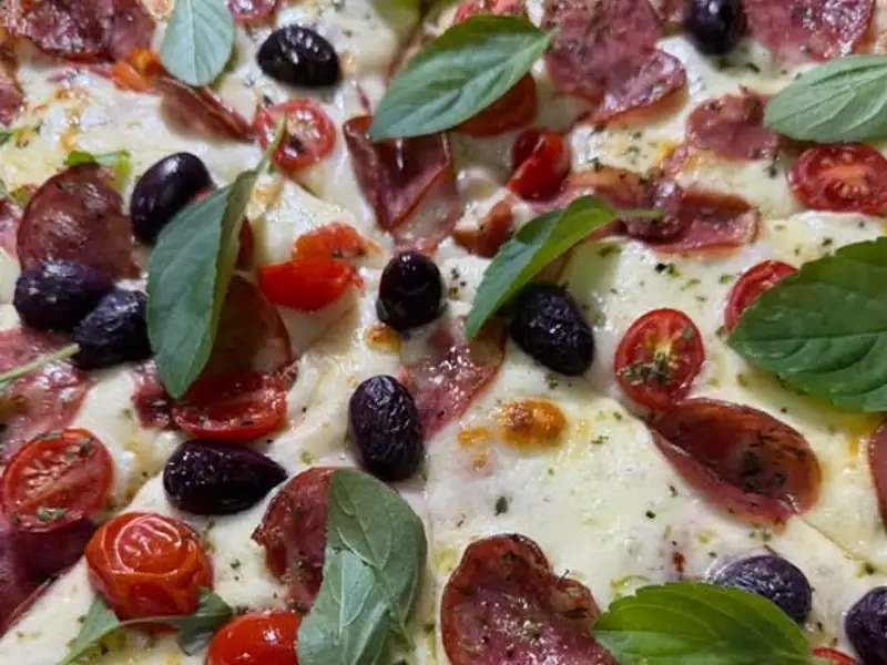 Pizza de mussarela com calabresa, tomate cereja, azeitonas pretas e manjericão