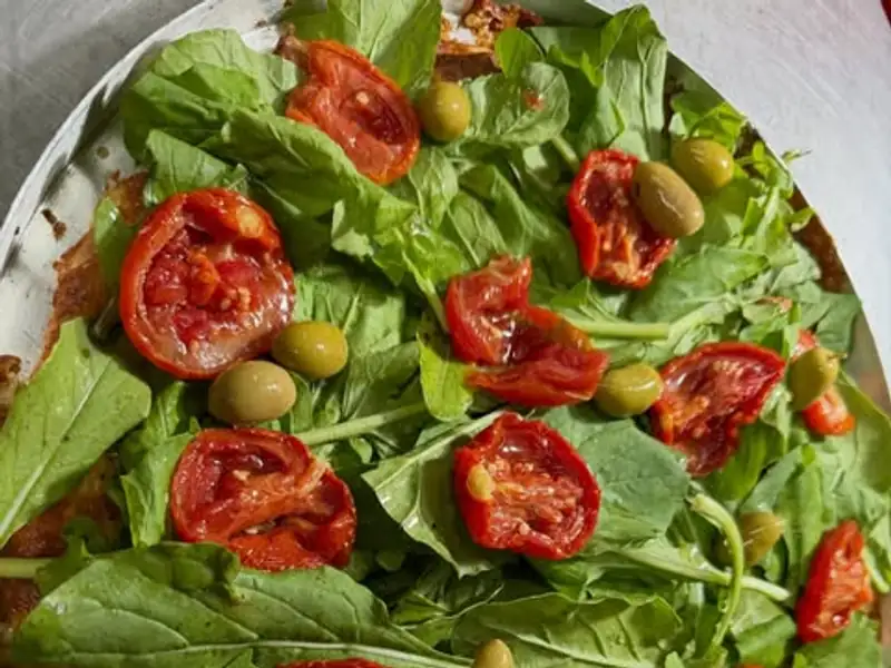 Pizza coberta de rúcula, tomate seco e azeitonas