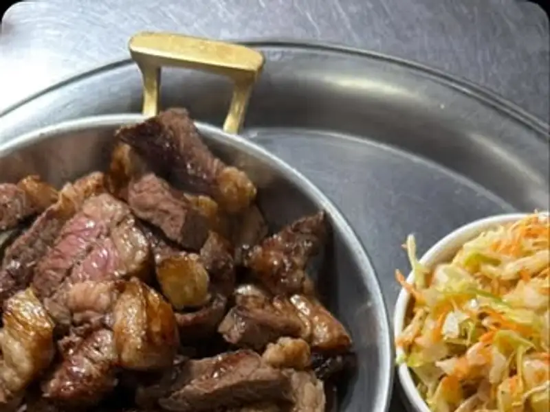 Carne em pedaços numa panela de ferro, com vinagrete e farofa ao lado
