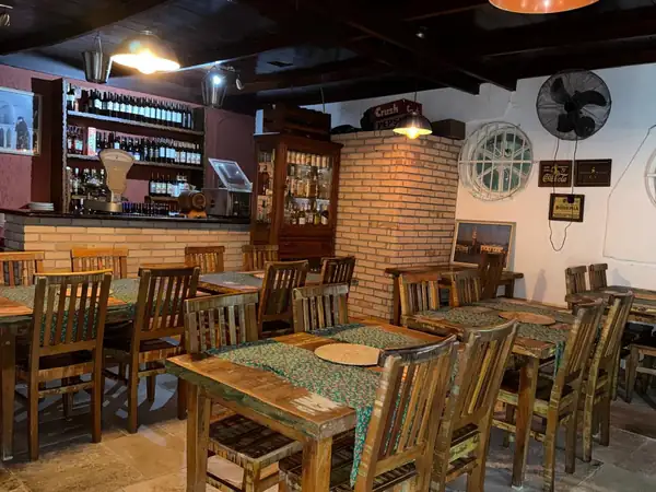 Salão de mesas de madeira rústica e balcão com prateleiras de vinho da Pizzaria Serena