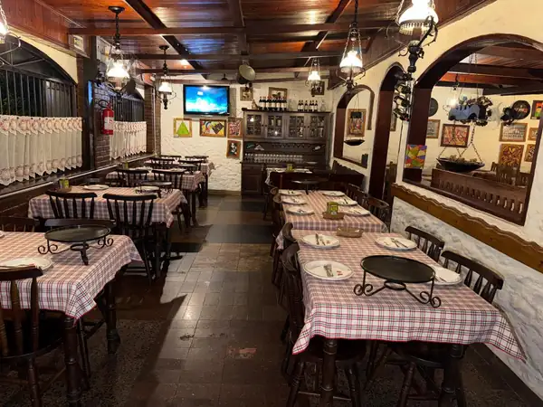 Salão com mesas de toalha xadrez, lustres e paredes de pedra da Pizzaria Serena